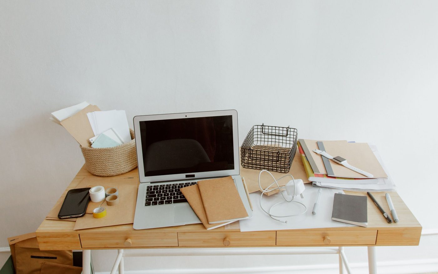 A wooden desk with a laptop, notebooks and paperwork