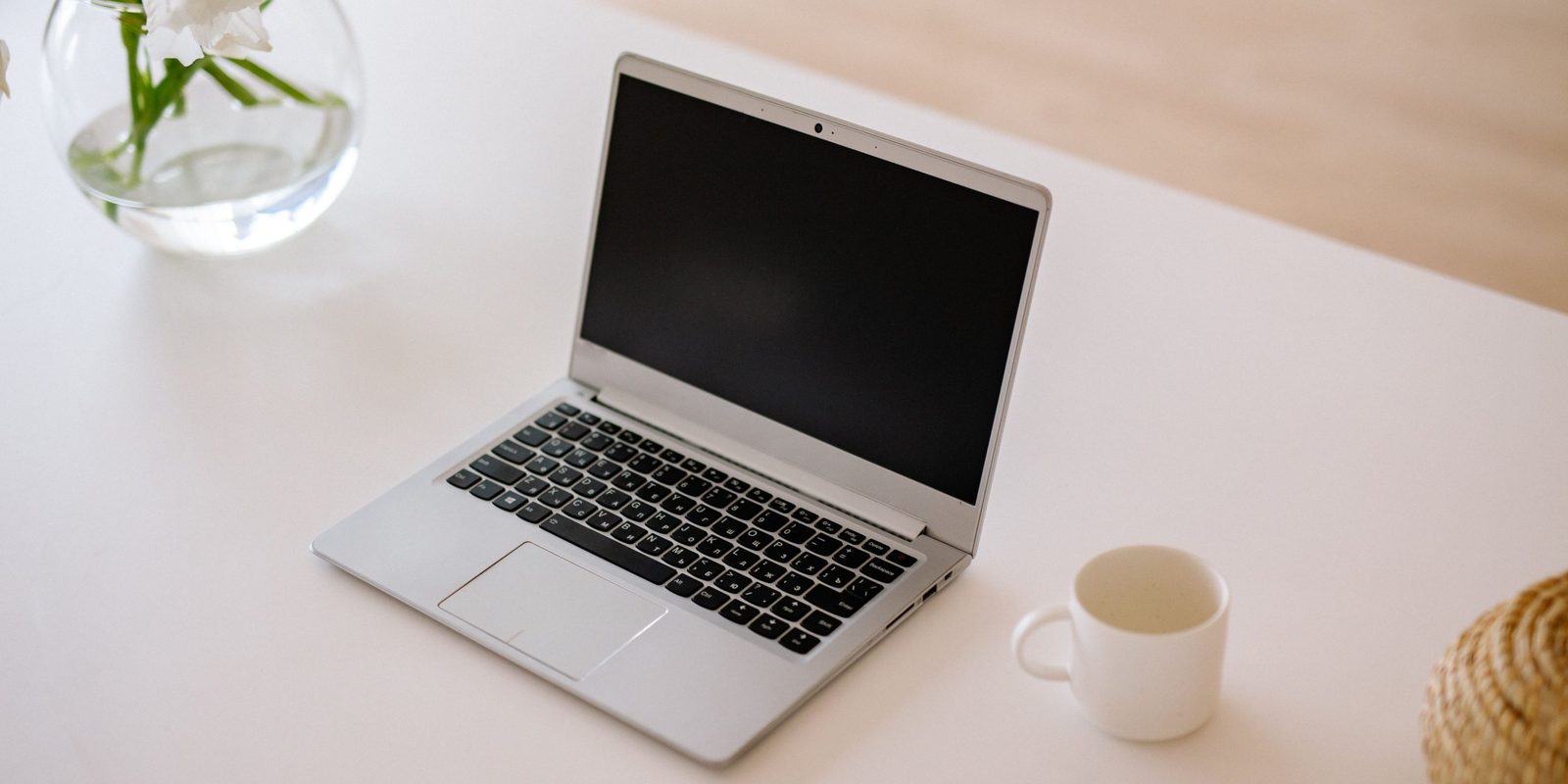 A calm white desk with a laptop and a cup