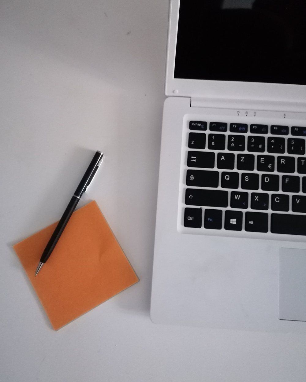 A pen resting on a sticky note beside a laptop